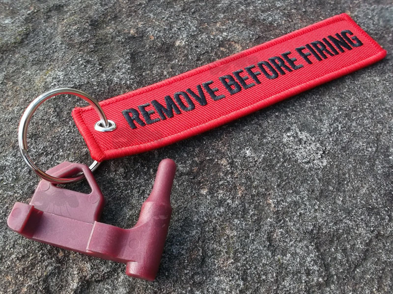 Maroon Coloured Plastic Universal Firearm Empty Chamber Safety Flag with Flathead Screwdriver and Rifle Rail Fitting, Fitted with a Red Canvas Flag with Black Embroidered Remove Before Firing Text